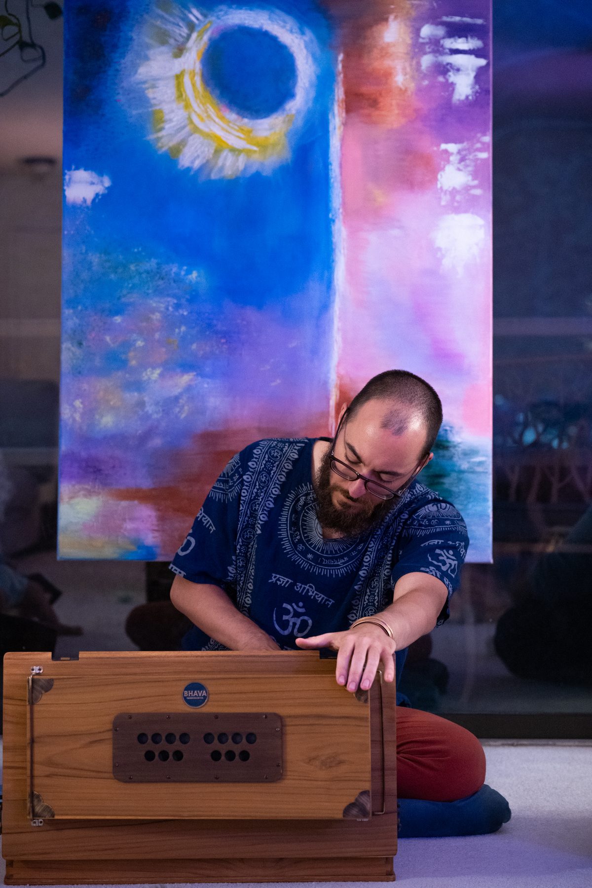 Mitchell Lessmann playing harmonium during a kirtan in front of a cosmic painting